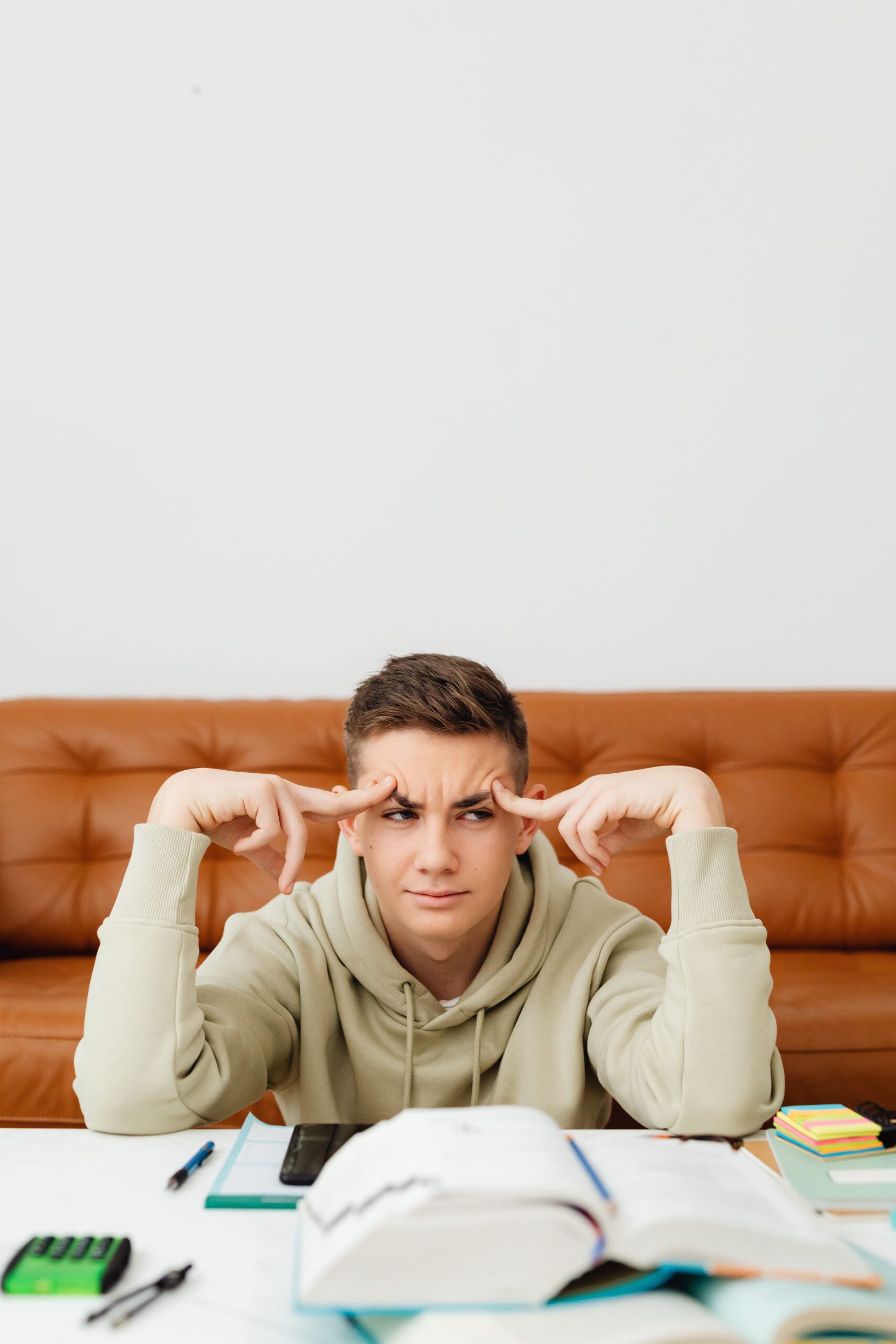 A teenager sits at home studying with a confused expression, surrounded by textbooks.